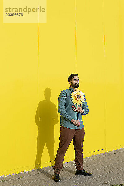 Man holding sunflower and standing in front of yellow wall