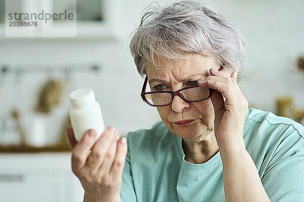 Focused senior woman reading medicine bottle at home