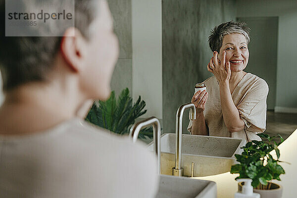 Smiling woman doing skincare looking in mirror at home