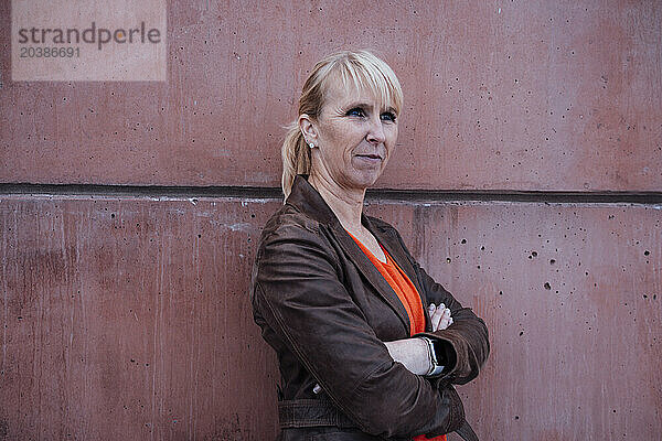 Smiling businesswoman leaning with arms crossed on wall