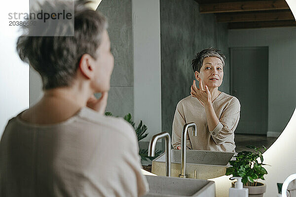 Woman taking care of skin looking in mirror at home