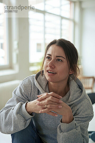 Thoughtful woman sitting with hands clasped at home