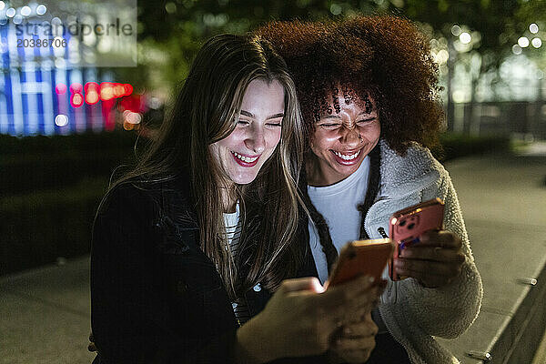 Happy young friends using smart phones at night