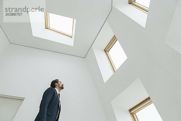 Businessman standing under skylight looking at window in office