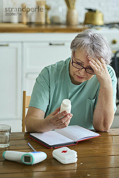 Worried woman with head in hand holding medicine bottle at home