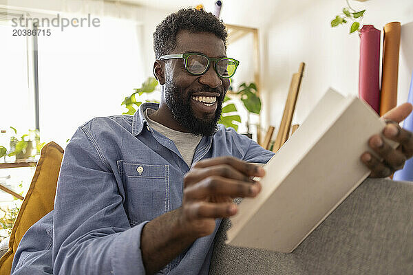 Happy non-binary person wearing eyeglasses and reading book at home