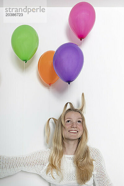 Blond teenage girl with multi colored balloons tied on hair