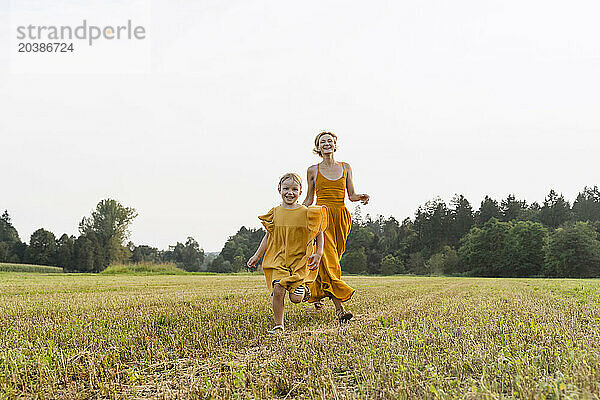 Playful mother and daughter running in meadow