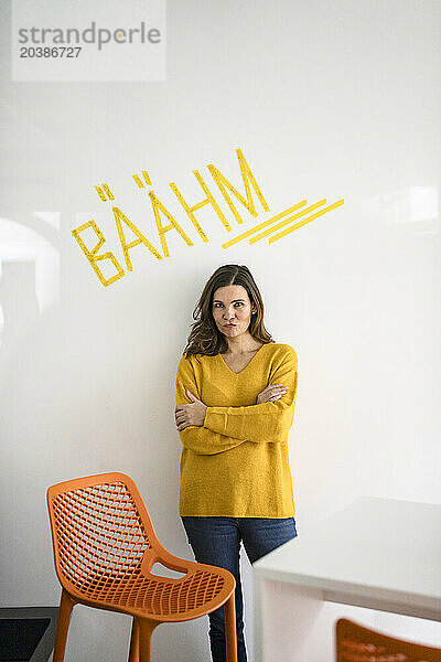 Creative businesswoman with arms crossed in front of white wall with text