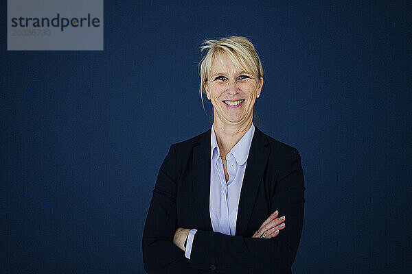 Smiling businesswoman standing with arms crossed against navy blue background