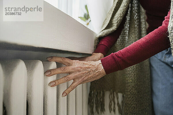 Hands of senior woman examining temperature of radiator at home