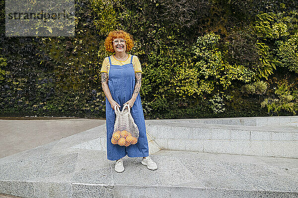 Smiling senior woman with oranges in mesh bag