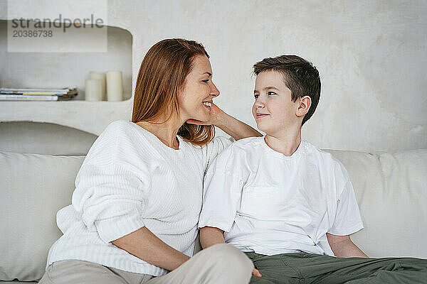 Happy woman and son sitting face to face on couch at home