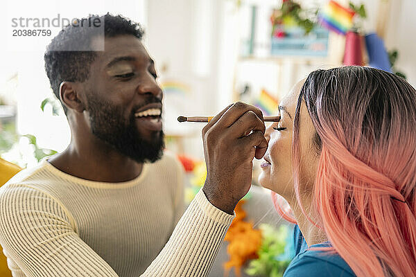 Young non-binary person applying make-up to friend with dyed hair at home