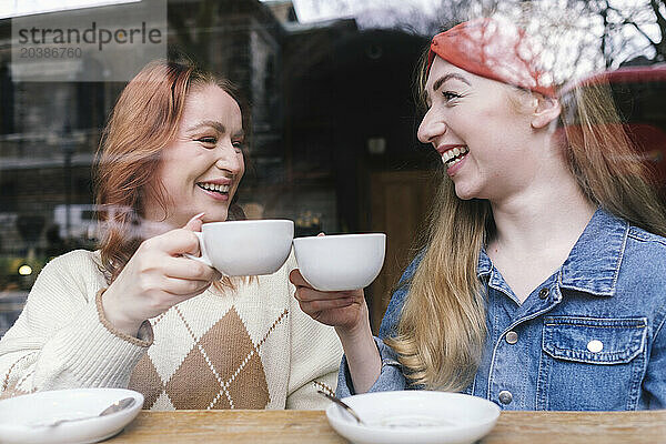 Cheerful friends toasting coffee cups in cafe