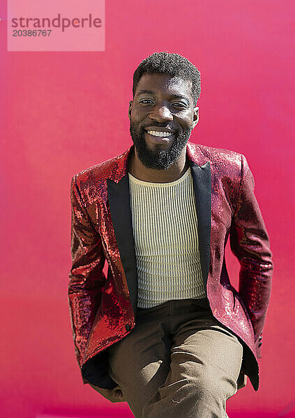 Smiling non-binary person wearing red blazer against pink background