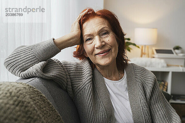 Smiling senior redhead woman sitting on couch at home