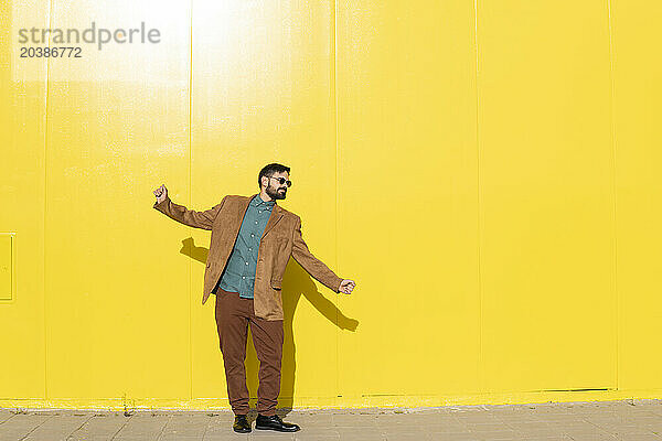 Man wearing sunglasses and dancing in front of yellow wall