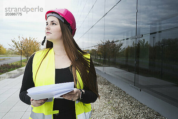 Thoughtful architect holding documents near building