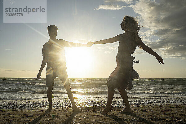 Back lit couple enjoying dance at windy beach