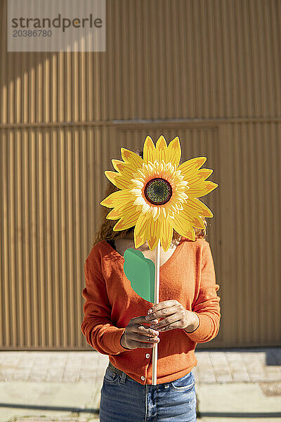 Young woman holding artificial sunflower in front of face