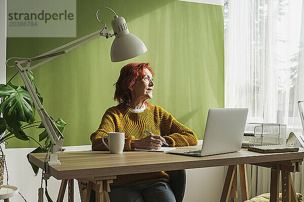 Thoughtful senior businesswoman sitting with laptop working at home