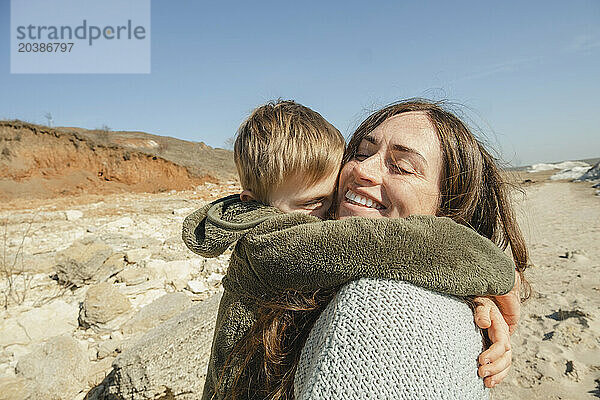 Boy embracing happy mother on sunny day