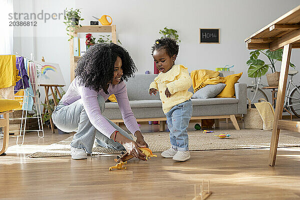 Happy mother kneeling with toys by daughter in living room at home