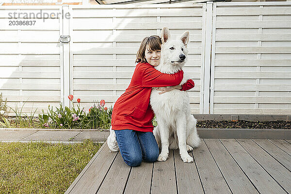 Smiling girl embracing white dog on porch of house