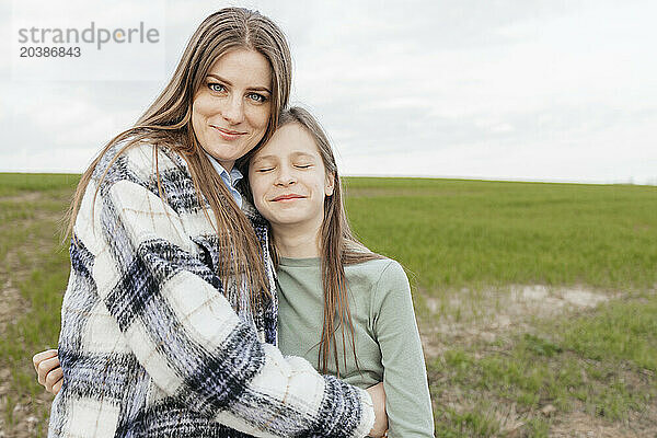 Smiling woman embracing daughter at meadow