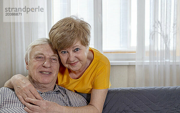 Smiling senior woman hugging man sitting on sofa at home