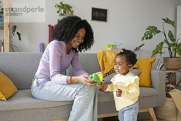 Happy mother and daughter playing with toy in living room