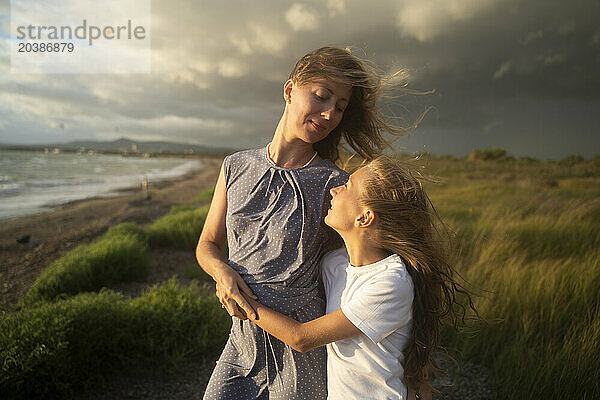 Blond mother and daughter hugging at windy beach