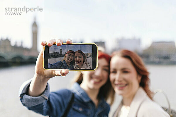 Smiling friends taking selfie through smart phone in city of London