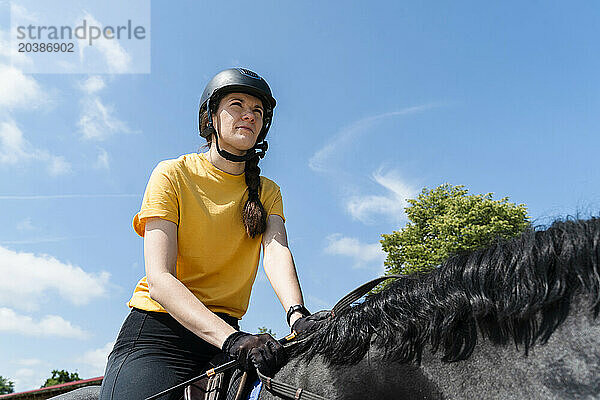 Confidence instructor riding black horse on sunny day