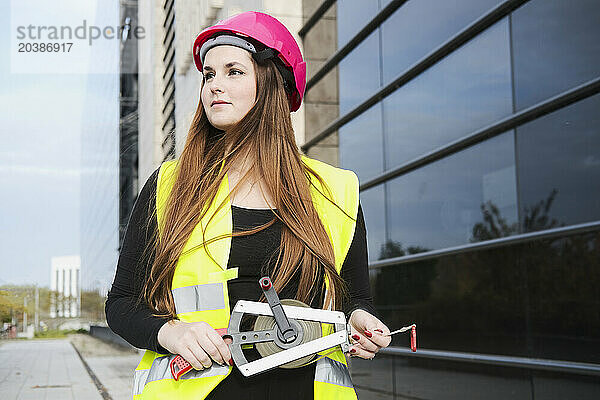 Thoughtful geodesist holding measuring tape near building