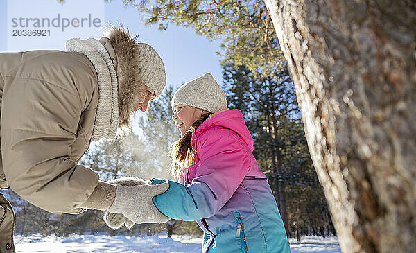 Mother and daughter holding hands and playing in winter forest on sunny day