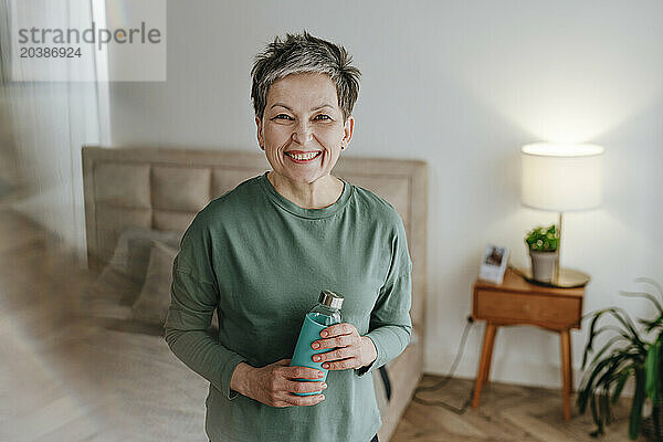 Happy mature woman holding water bottle at home