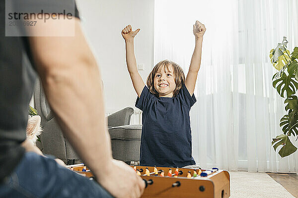 Cheerful boy playing foosball with father at home