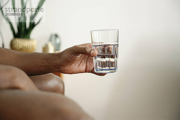 Man's hand holding glass of water in bedroom at home