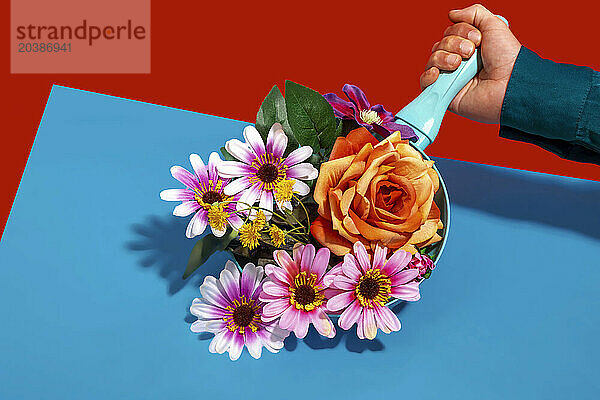 Hand of man holding frying pan with colorful flowers against colored background