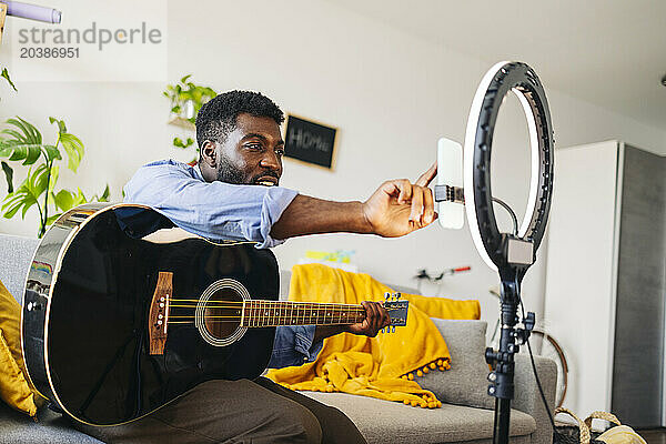 Influencer using mobile phone and sitting with guitar at home