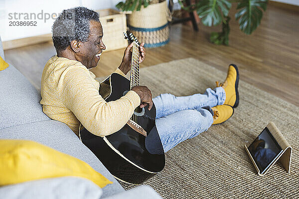 Happy senior man learning guitar online on tablet PC