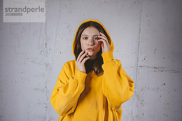 Girl in yellow hoodie posing in front of gray background