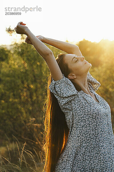 Beautiful woman stretching in field at sunset