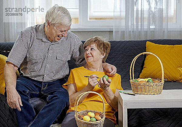 Elderly woman painting Easter eggs near happy man at home