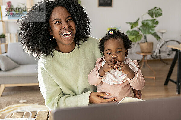 Cheerful young woman sitting with daughter in living room at home