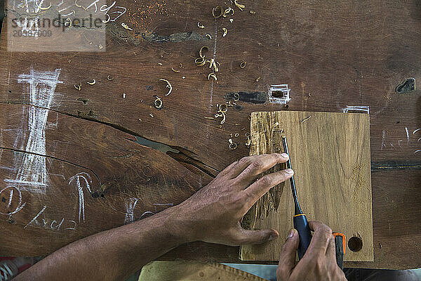 Hands of carpenter carving wooden piece on workbench at workshop