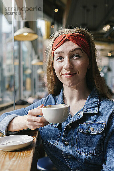 Smiling young woman sitting with coffee cup in cafe