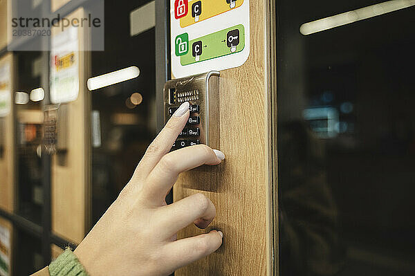Hand of woman entering password on keypad of locker at supermarket